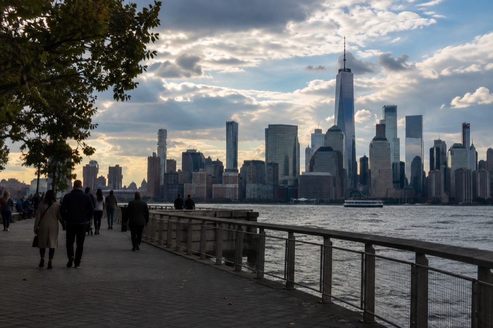 A pedestrian promenade with the Manhattan skyline behind it in late afternoon light