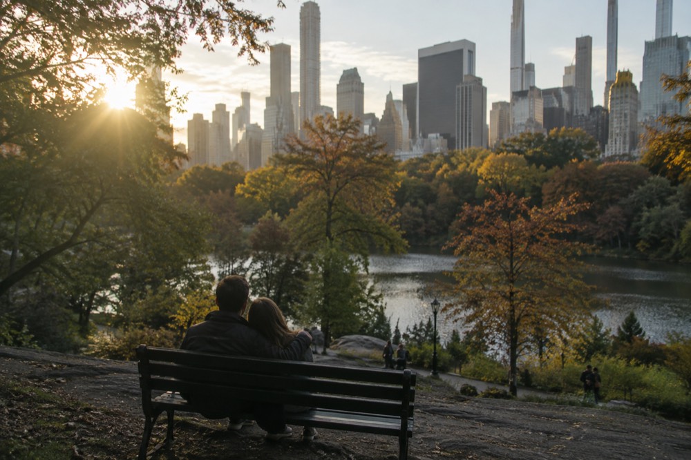 A couple resting on a Central Park bench with the skyline rising behind the trees