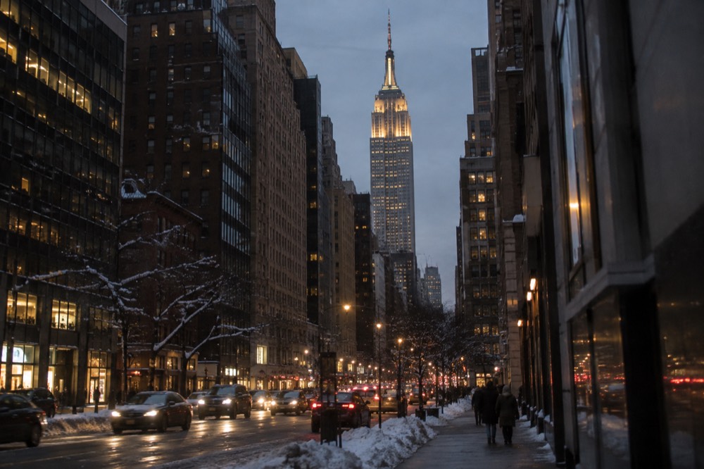 The illuminated Empire State Building seen from a snowy Midtown street at dusk