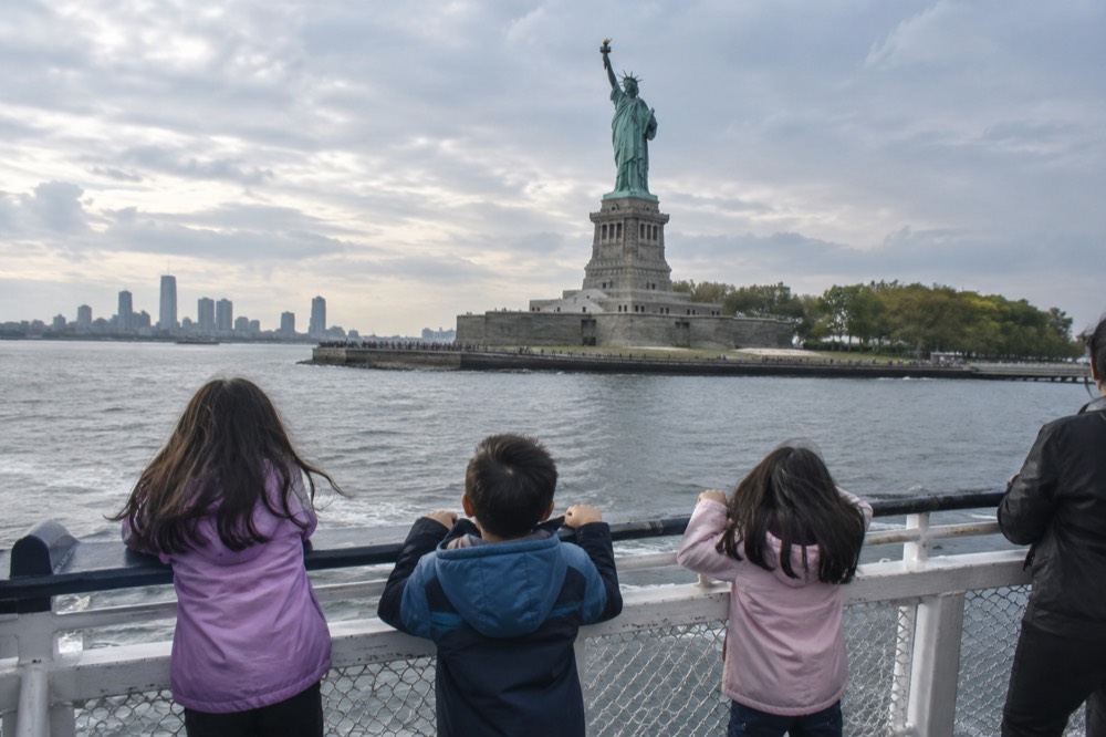 A ferry boat passing close to the Statue of Liberty with children at the rail
