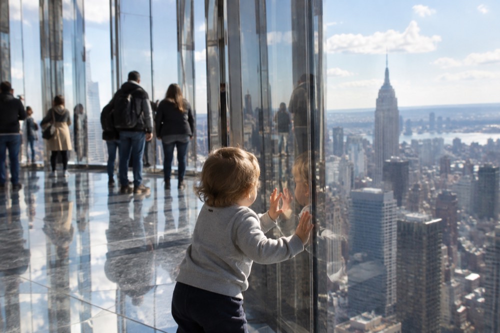 A child pressing hands against a mirrored wall in a bright observation deck room