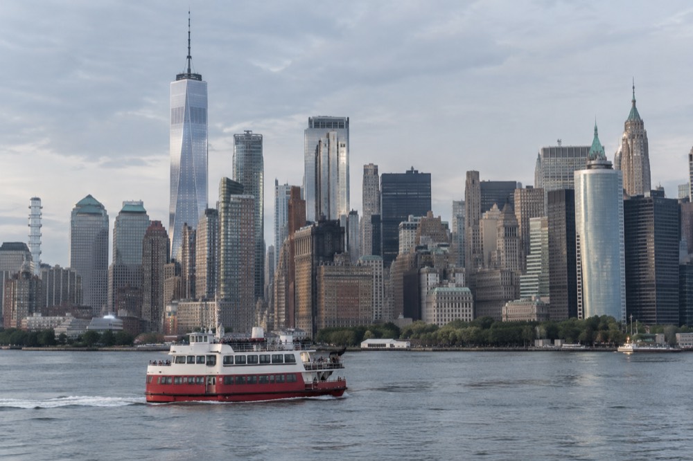 A red-and-white ferry crossing the harbor with the Lower Manhattan skyline behind it