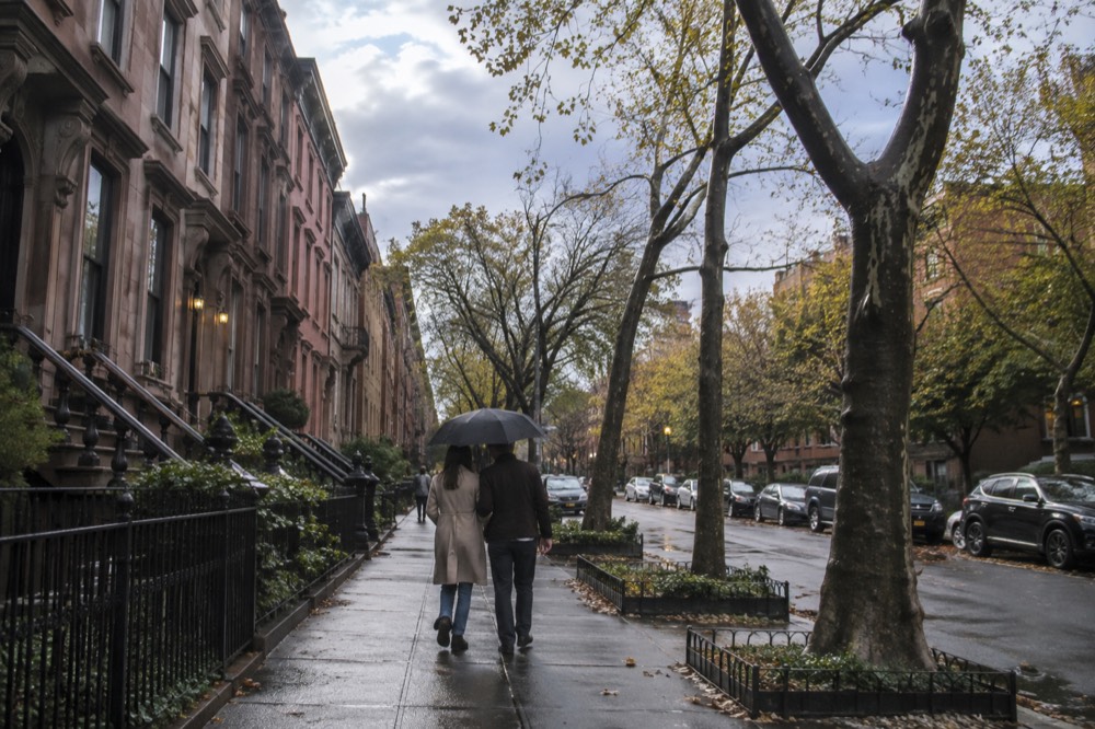 Two people sharing an umbrella on a quiet Greenwich Village street with brownstones behind them